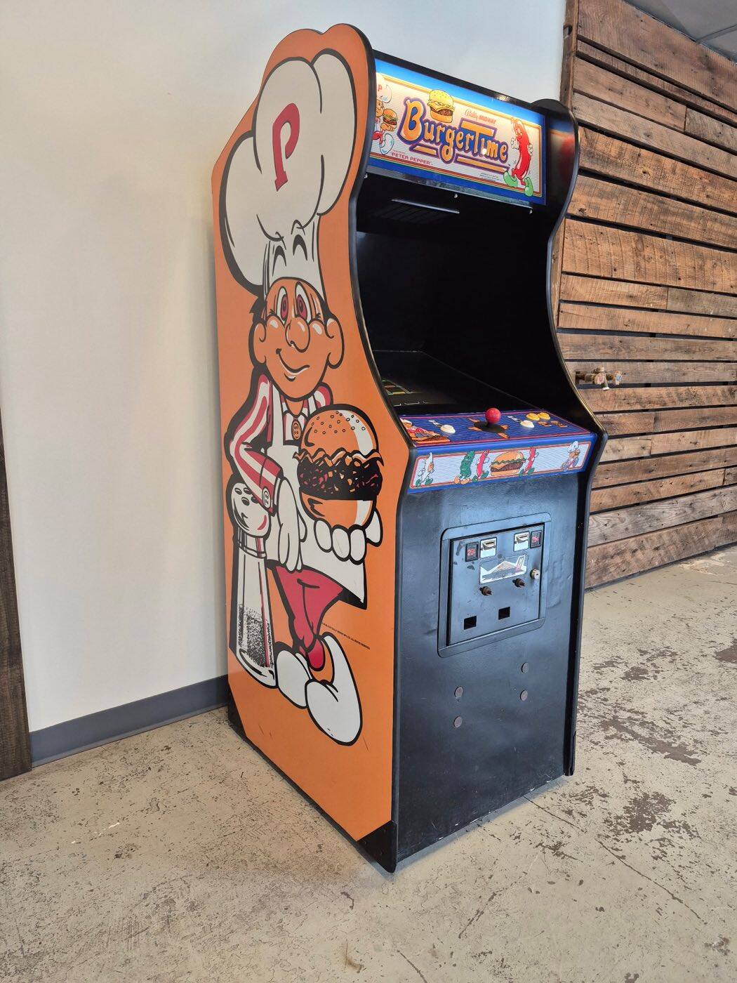 A vintage BurgerTime arcade cabinet with Peter Pepper side artwork against a reclaimed-wood wall inside Flip Side Burger Bar