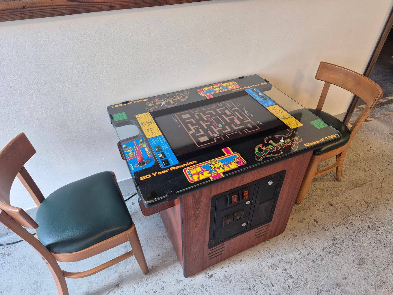A sit-down Ms. Pac-Man and Galaga cocktail arcade table with two chairs along the wall inside Flip Side Burger Bar