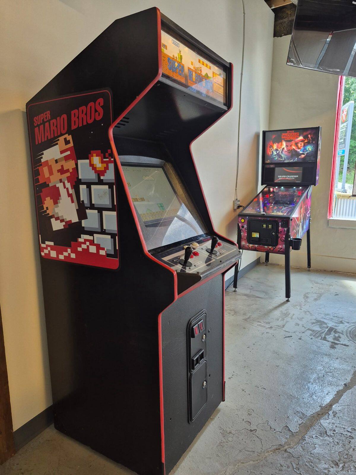 A Super Mario Bros arcade cabinet beside a Stranger Things pinball machine in the game corner at Flip Side Burger Bar