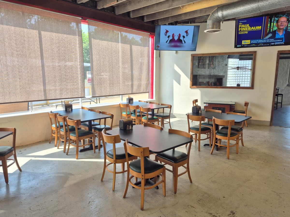 Dining room at Flip Side Burger Bar with wooden chairs, dark tables, roller shades, and TVs on the wall
