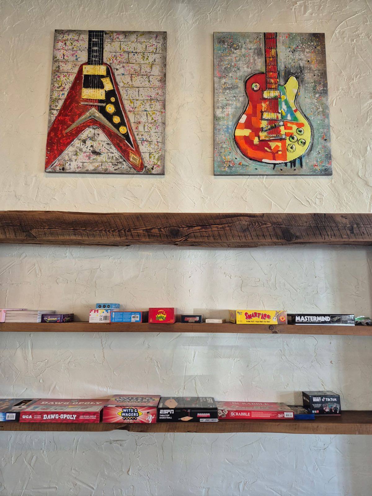 Hand-painted guitar artwork above reclaimed-wood shelves stacked with board games, including Scrabble and Mastermind, inside Flip Side Burger Bar