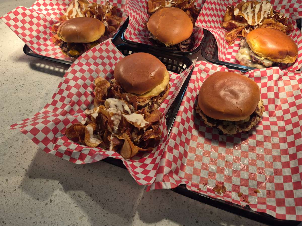 Five baskets of smash burgers and Tallow Chips lined up on the counter at Flip Side Burger Bar
