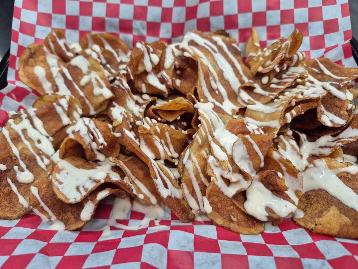 A basket of Tallow Chips &mdash; potato chips fried golden in tallow and drizzled with house-made Chipotle Ranch, served on red-and-white checkered paper