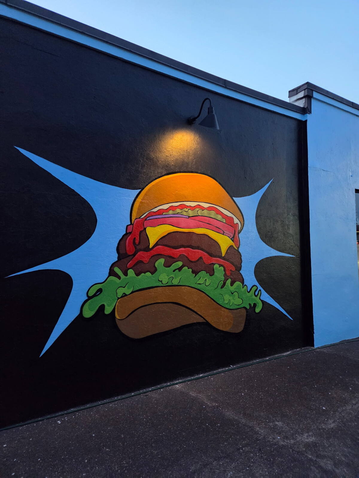 Full view of the hand-painted mural on Flip Side Burger Bar's black exterior wall, showing the cartoon burger and blue starburst from floor to roofline